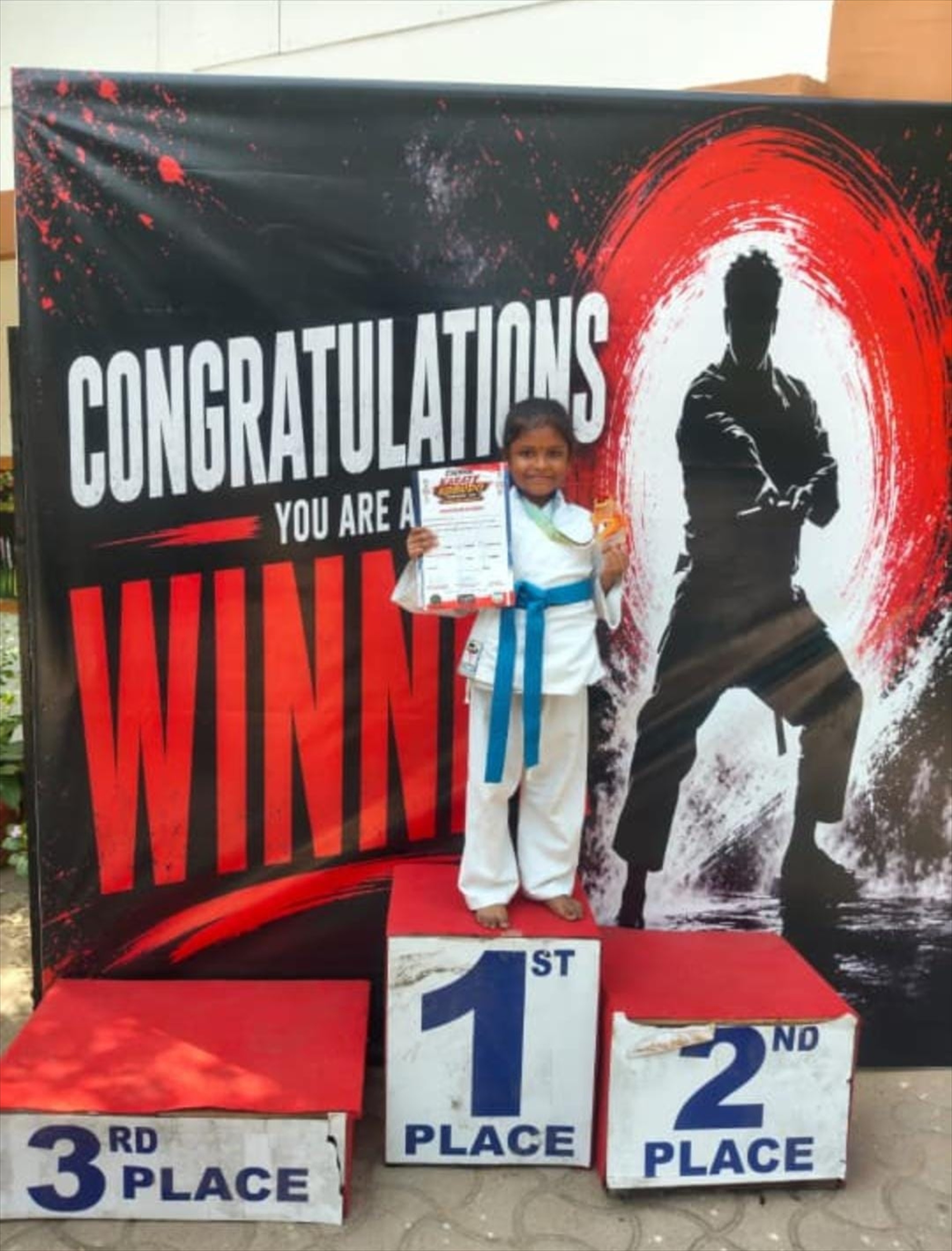 Young Darkan karate student standing on the first-place podium with a medal and certificate
